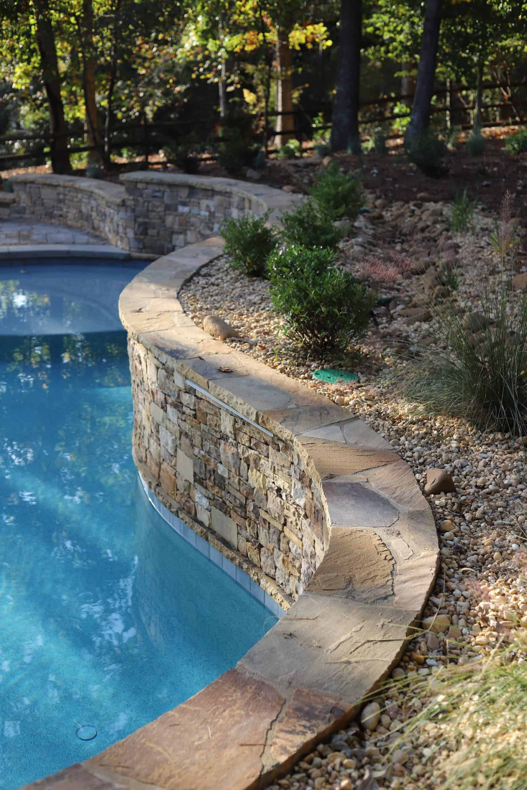 Pool edge with natural stone and stone wall for a seamless outdoor look.