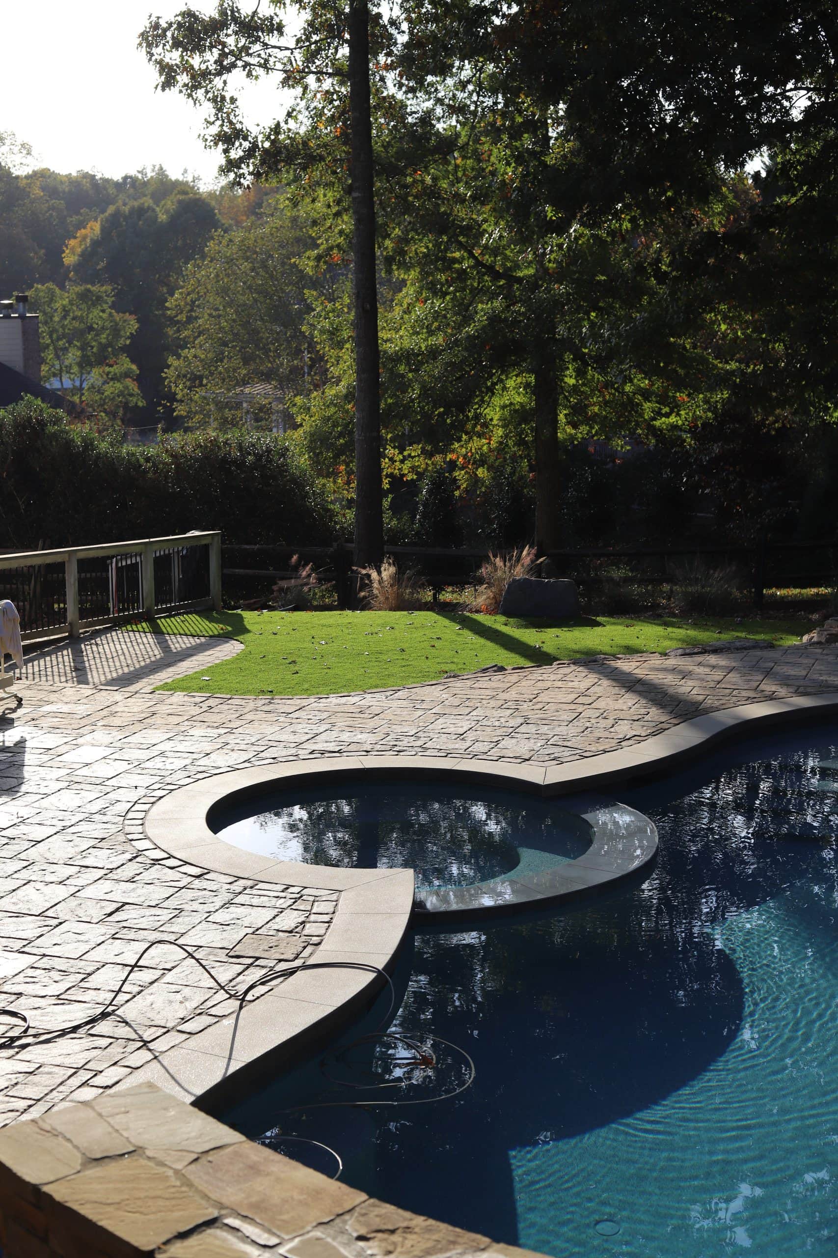 Outdoor swimming pool with a stone patio, surrounded by lush greenery and tall trees. Perfect for re.