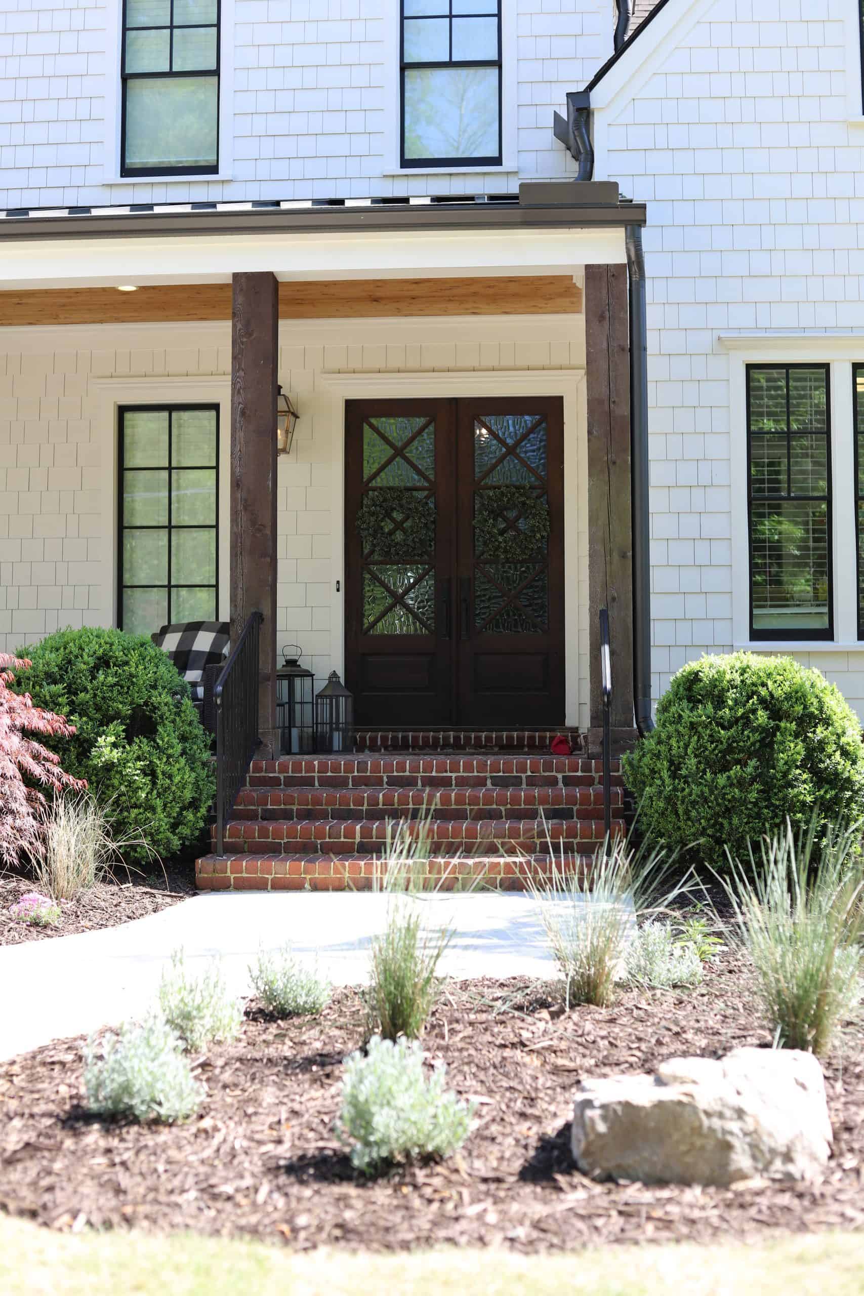 Landscaped front entry of the Healy Project featuring clipped boxwood topiaries, ornamental grasses, brick columns, and reclaimed wood porch beams on an Atlanta estate home