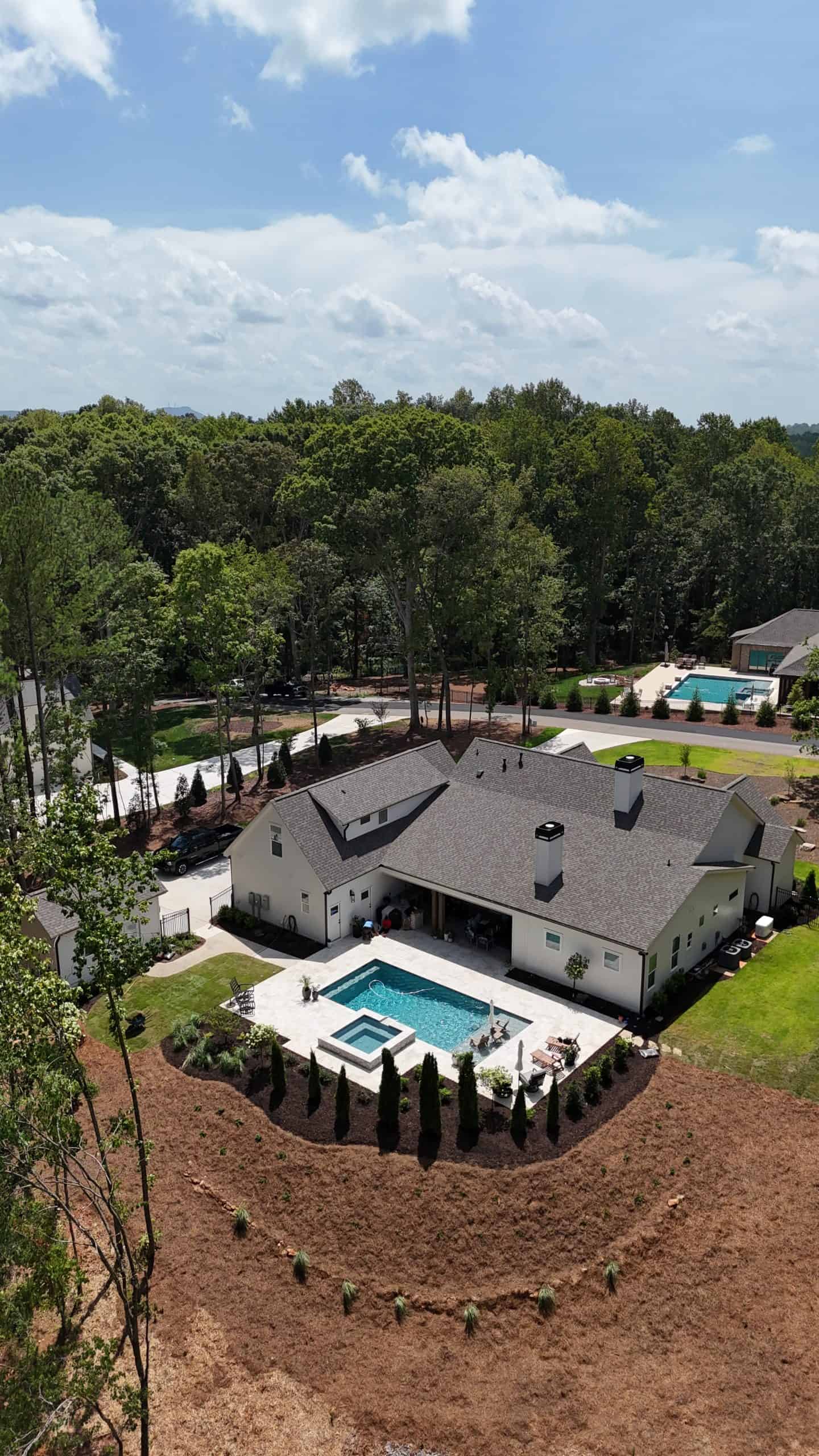 Aerial drone view of the Burras Oak Lane project featuring a rectangular pool with spa, limestone pool surround, Italian cypress plantings, and estate landscaping surrounding a white modern farmhouse in Atlanta