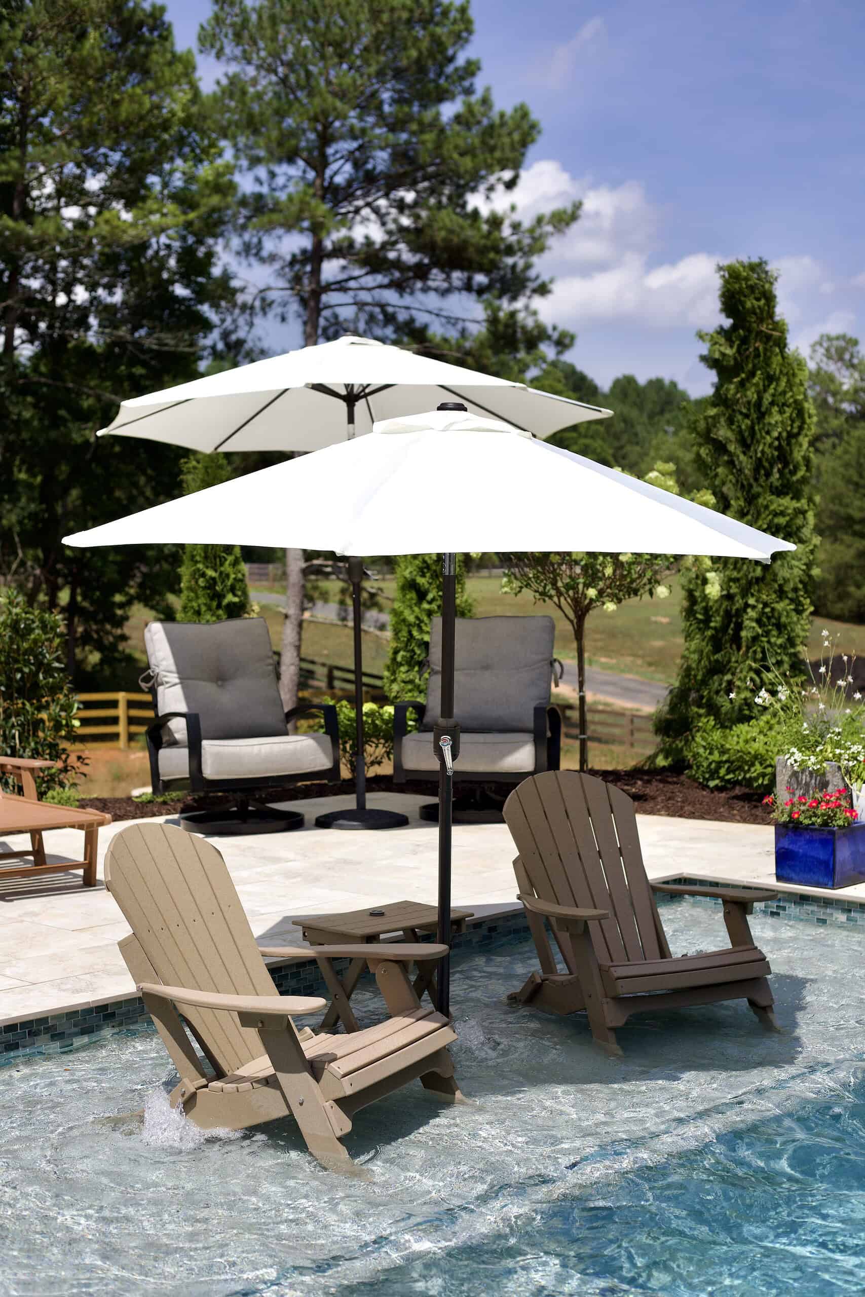 Luxury pool outdoor living area at Burras Oak Lane featuring in-pool Adirondack chairs, market umbrellas, travertine pool surround, Italian cypress trees, and mixed ornamental planting beds designed by Garden Atlantic in Cumming, Georgia