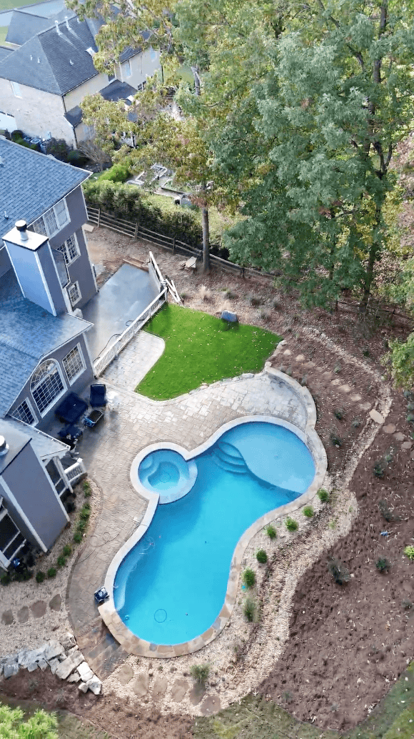 Aerial drone view of a Cumming, Georgia backyard featuring a freeform pool with integrated spa, flagstone patio surround, zoysia lawn, boulder retaining walls, and naturalistic planting beds installed by Garden Atlantic