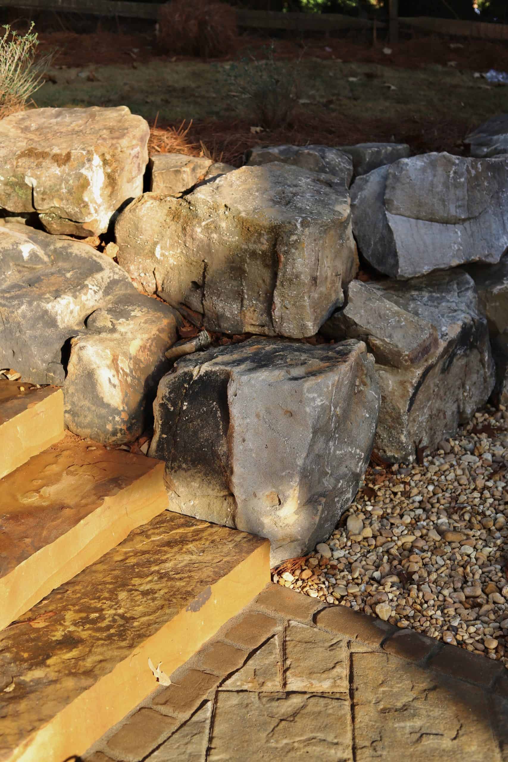 Close-up detail of natural fieldstone boulder retaining wall with amber flagstone steps and pea gravel ground cover at a Cumming, Georgia estate installed by Garden Atlantic