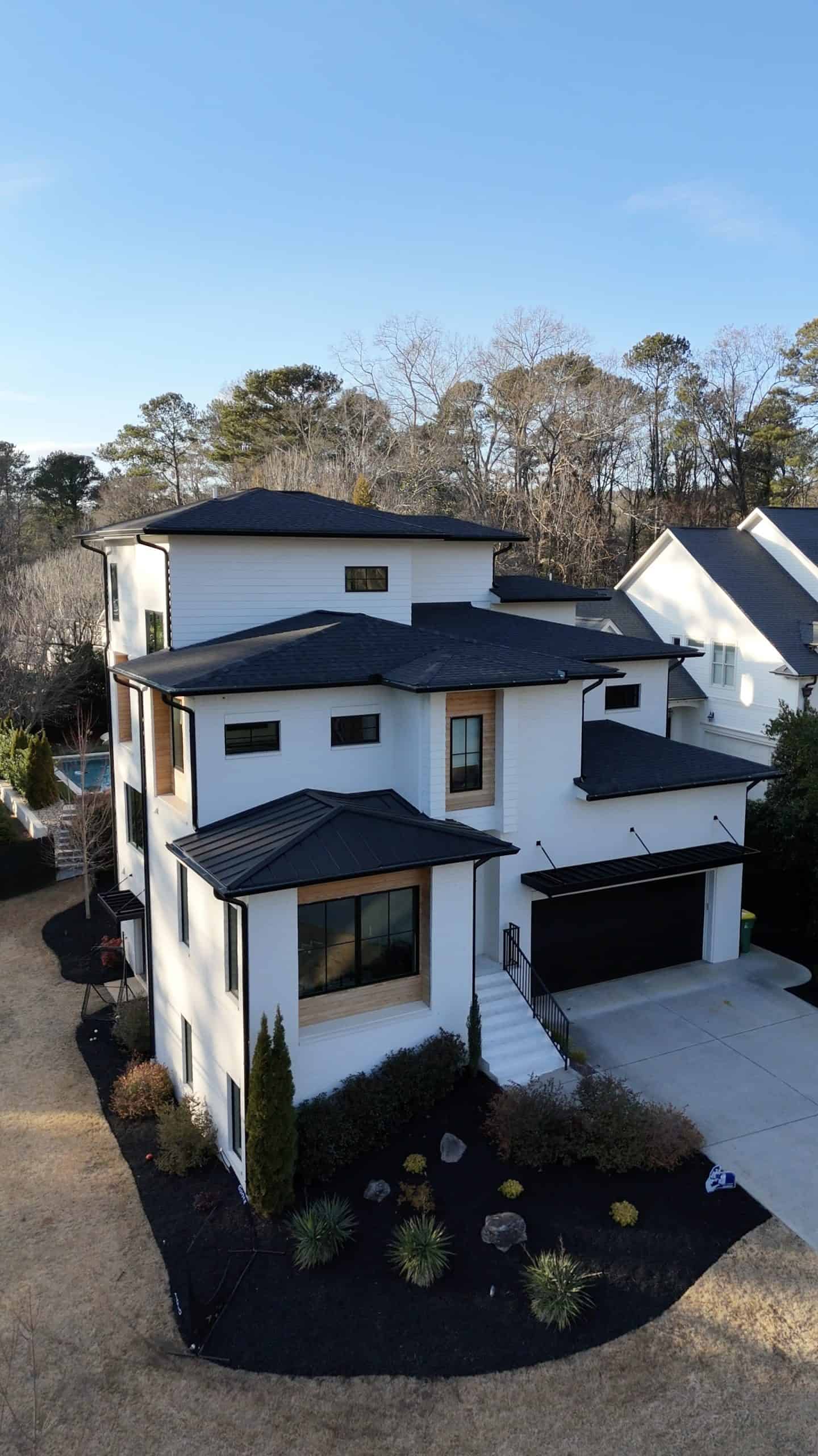 Aerial view of a three-story modern white brick home in Sandy Springs, Georgia with dark mulch planting beds, columnar arborvitae, barberry, yucca, and fieldstone boulders framing the front entry, designed by Garden Atlantic