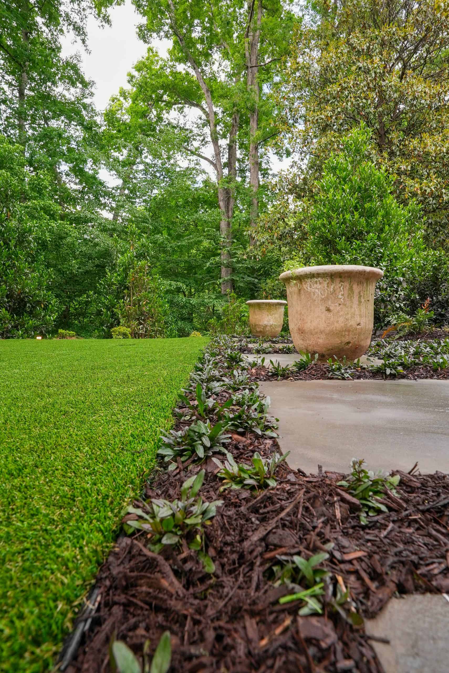 Weathered stone garden urns beside a manicured synthetic-turf lawn and planted border in a Buckhead estate garden.